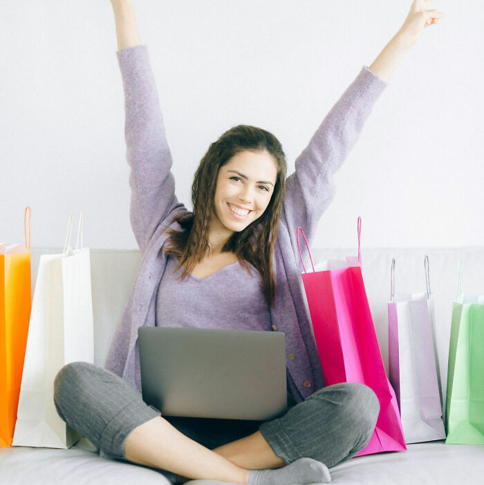 Happy woman sitting with a laptop surrounded by colorful shopping bags, illustrating smart life tricks for online shopping.
