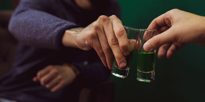 Two people clinking shot glasses filled with green liquid, unexpected non-candy items during trick-or-treating.