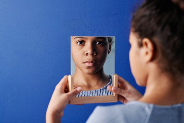A young child looking into a small framed mirror instead of receiving trick-or-treating candy.