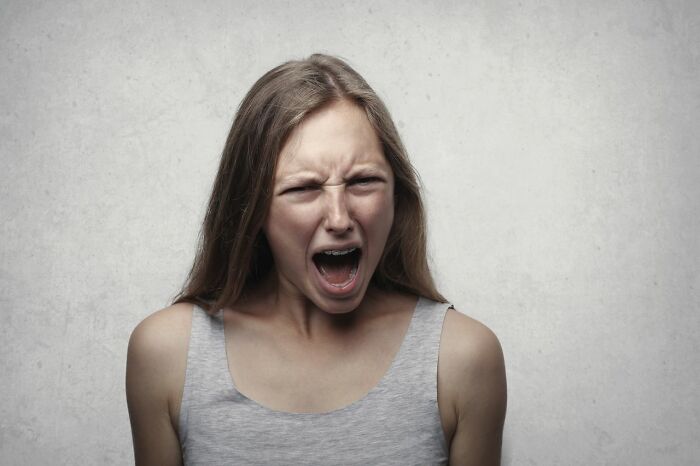 Young woman yelling with anger against neutral background