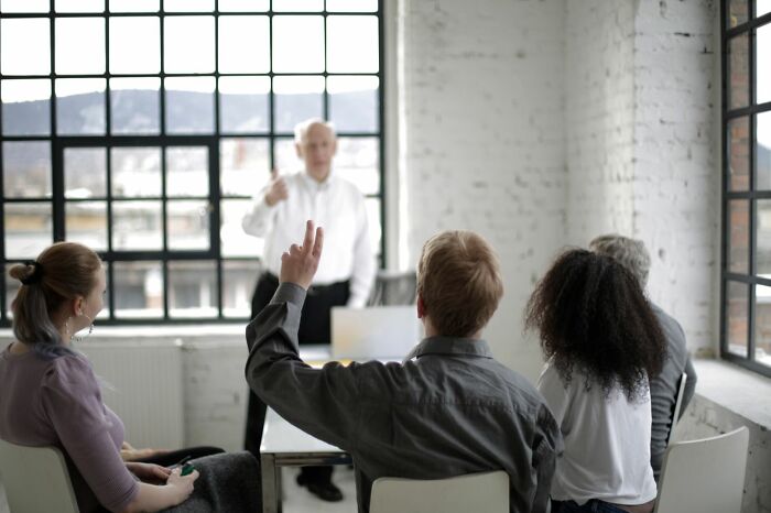 A man raises his hand during a meeting, showcasing clever life tricks for effective communication.