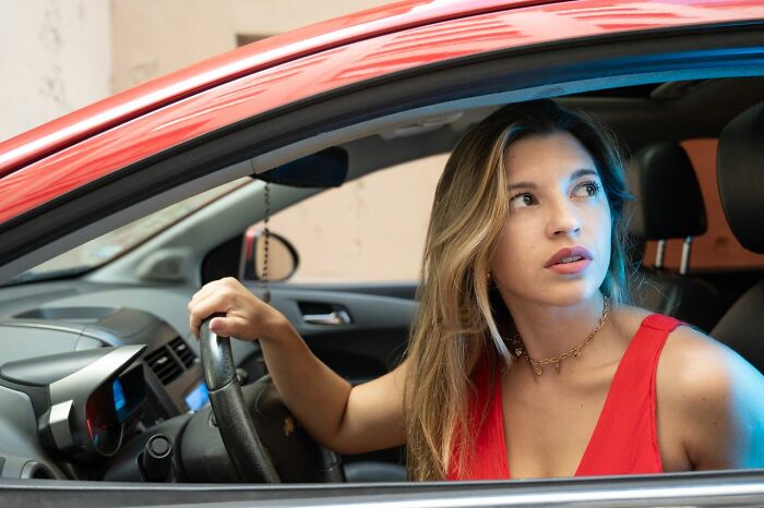A worried young woman behind the steering wheel of her car, struck by an urgent feeling to leave