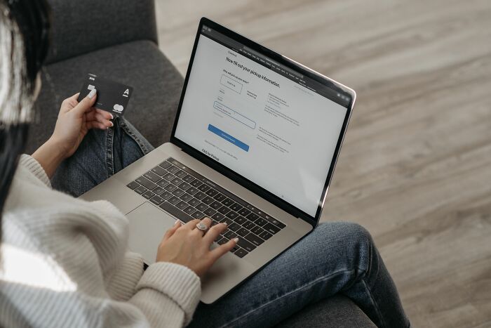 A woman holding a credit card while typing on her laptop, depicting unethical life pro tips for online shopping