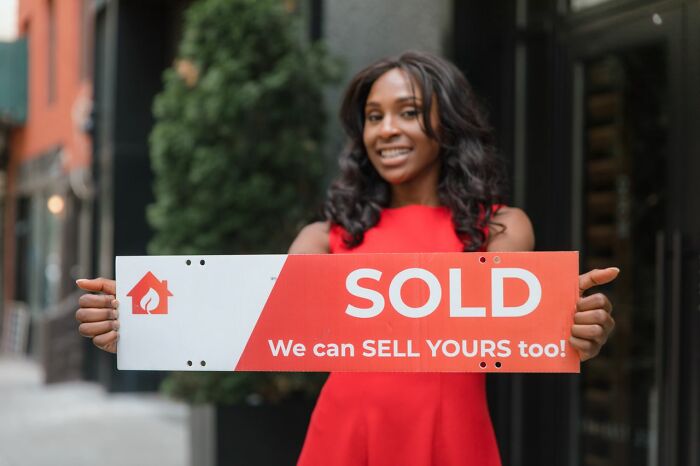 A woman holding a sold sign illustrating what happens when men walk away from their marriage.