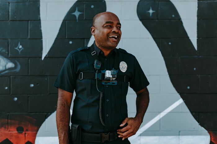 Police officer wearing body camera standing in front of mural and smiling