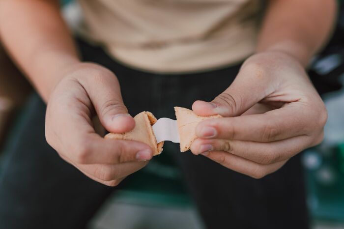 Hands breaking open a fortune cookie, revealing paper inside instead of sweet trick-or-treating candy.