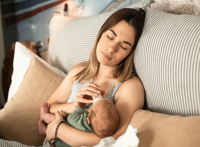 Tired woman bottle feeding a newborn, highlighting things women wish they knew about early motherhood.