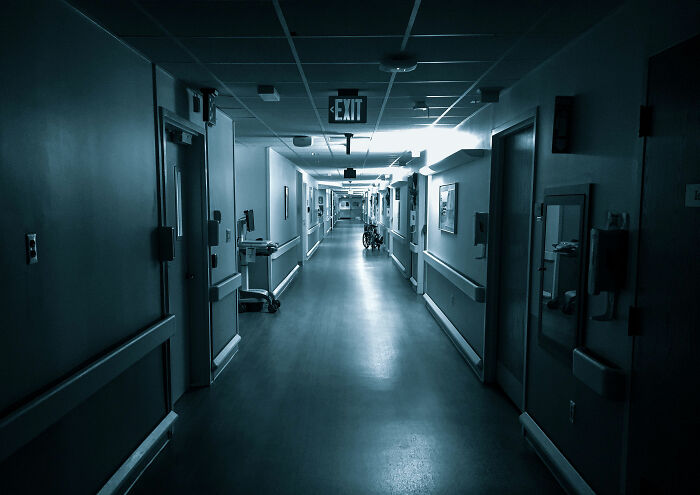 A dimly lit, empty hospital corridor leading to a door with an exit sign.