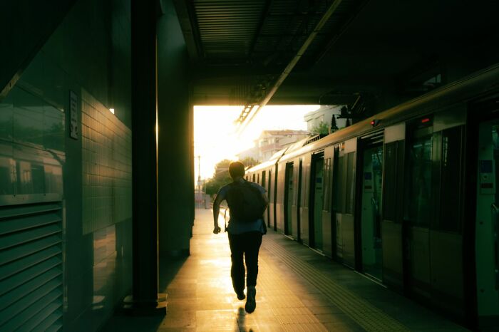 A man running on a train platform during sunset, capturing the urgent feeling of leaving immediately