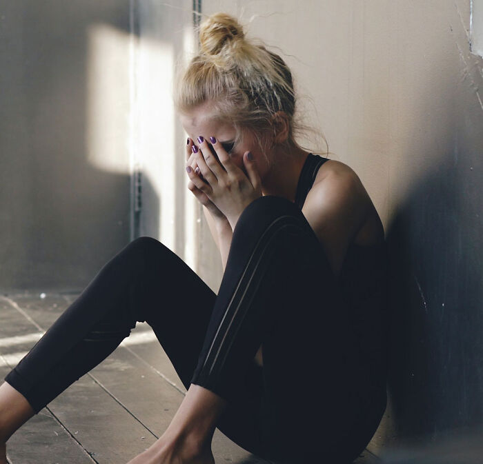 A distressed teen girl sitting on the floor covering her face with her hands