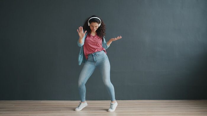 Woman wearing headphones happily dancing after reading about funny instances online.