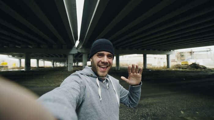 Happy man in beanie waving under a bridge, relating to satisfying revenge stories.
