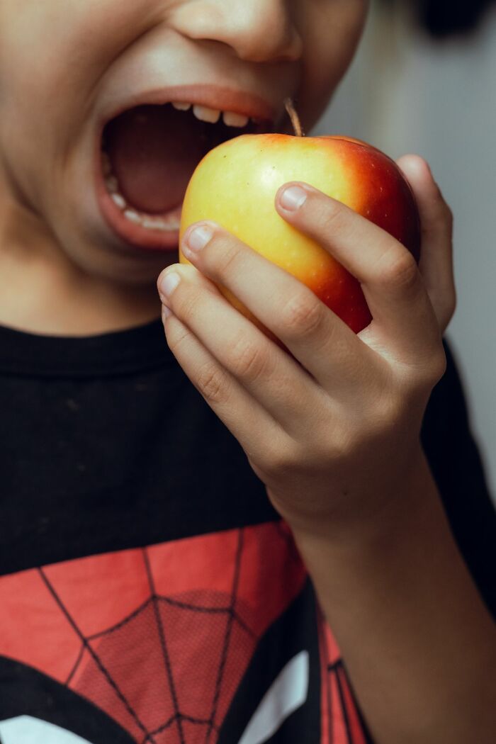 A child opening wide to bite into a fresh apple instead of receiving candy while trick-or-treating.