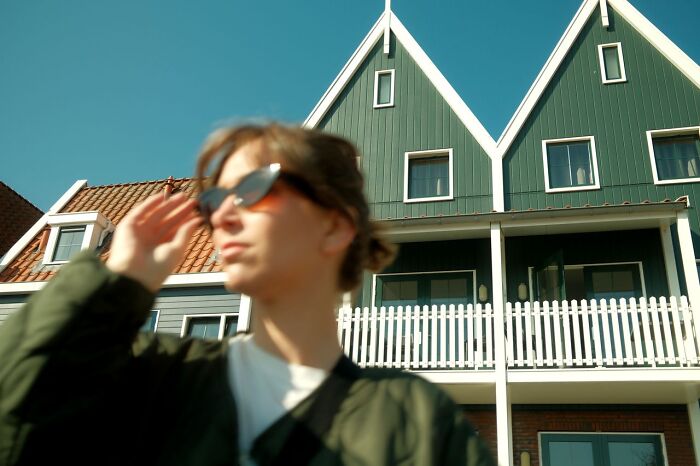 A woman wearing sunglasses standing outside modern houses, symbolic of residential family feuds.