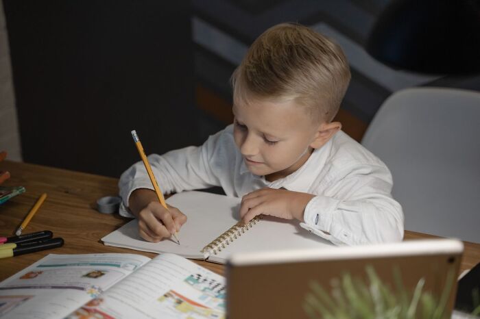 A young boy writing carefully in a notebook at a desk during homework time, related to family feuds.