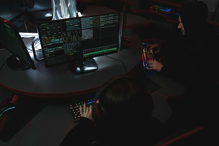 Two computer programmers working in a dark room with multiple monitors