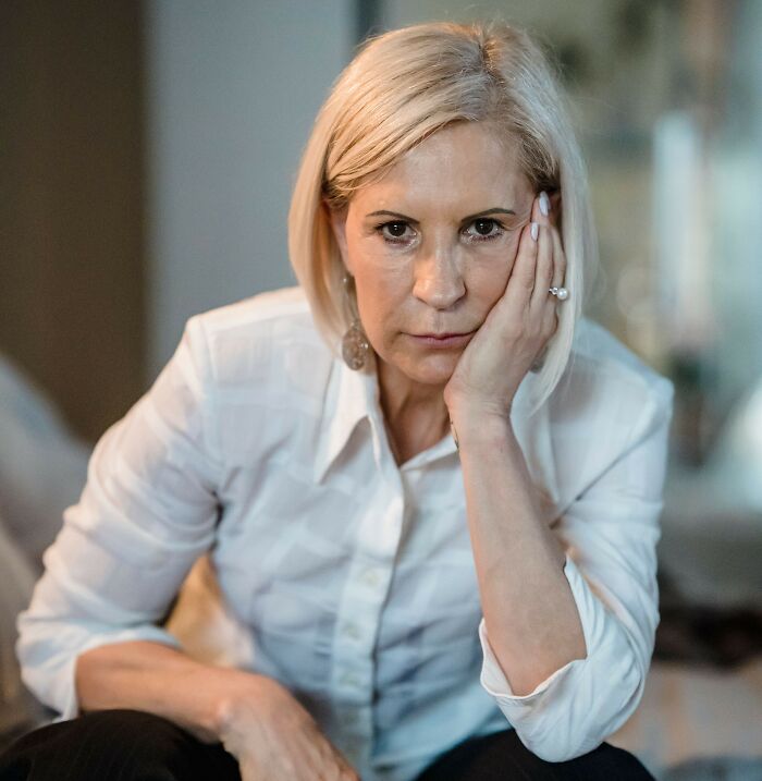 A serious blonde woman leaning her face on her hand.