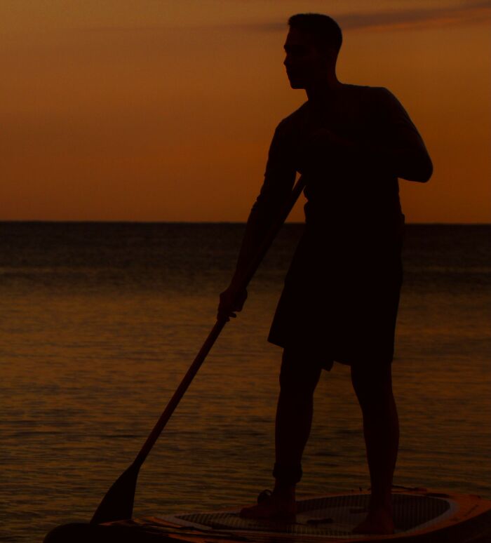 Silhouette of a man paddleboarding during sunset, reflecting chilling stories of gut feeling.