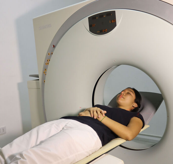 A young woman lying down in a medical scanner to examine broken ribs after a hug