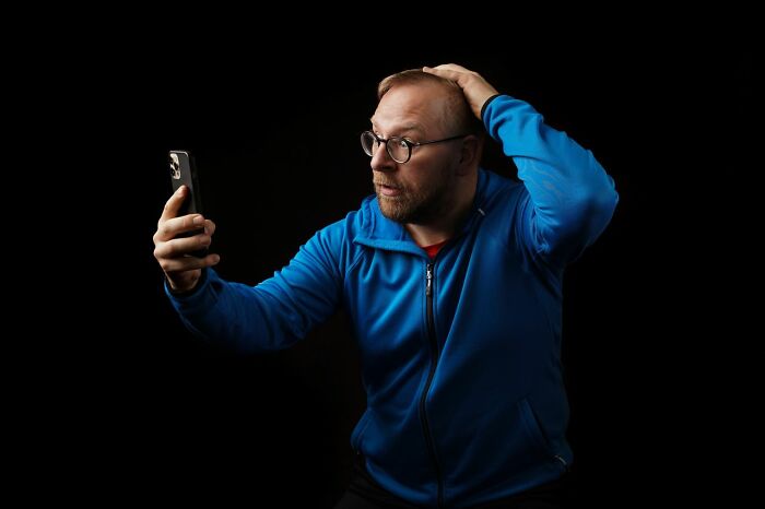 Surprised man holding his smartphone in shock after witnessing funny instances on screen.