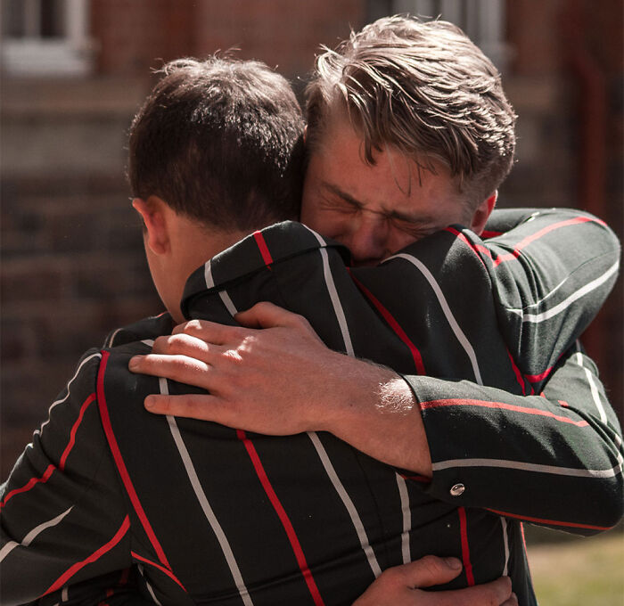 Emotional student hugging another person tightly outdoors.