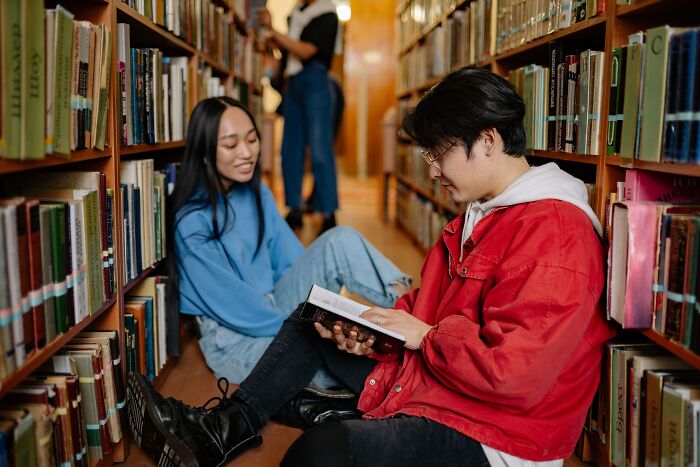 Students testing their general knowledge while sitting on the library floor reading books together. Students testing their general knowledge while sitting on the library floor reading books together.