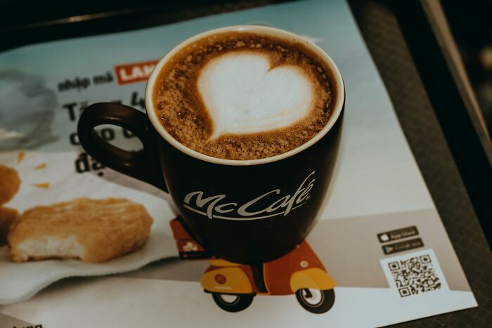 A black McCafé coffee cup with heart latte art, showcasing clever PR stunts branding.