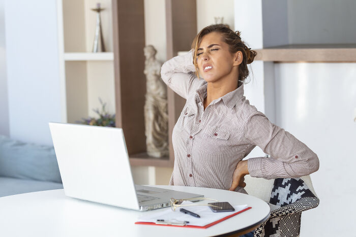 Woman stretching her aching back while working at a laptop, a common health problem in Gen Z.