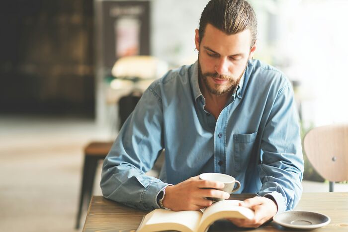 A man reading a book attentively in a cafe, reflecting positive masculinity.