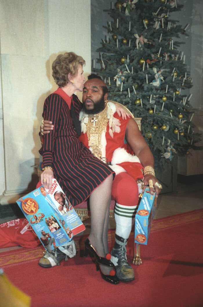 Nancy Reagan kissing Mr. T on the head near a Christmas tree, showing a festive moment of positive masculinity.