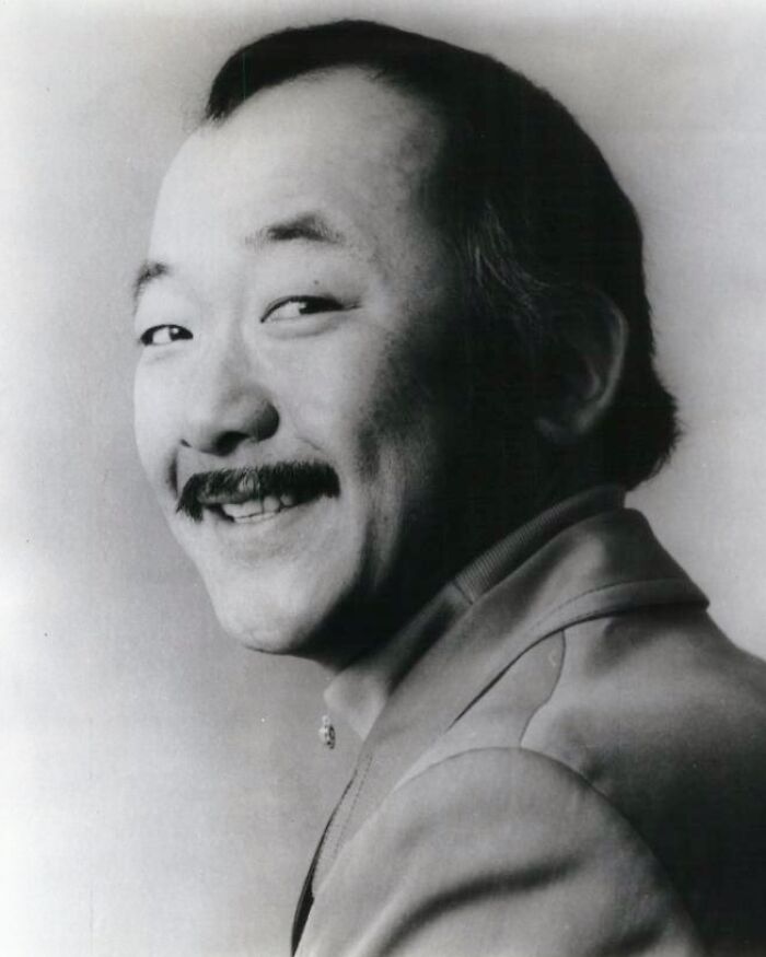 A black-and-white portrait of a smiling man with a mustache, demonstrating positive masculinity and warmth.