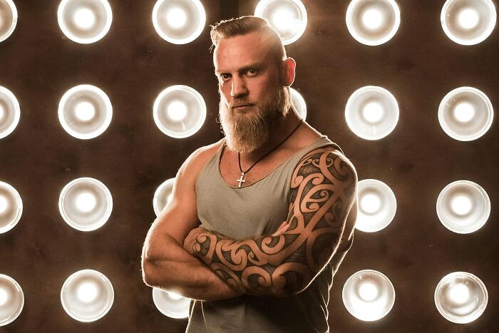 Strong bearded man with tattoos showing positive masculinity by standing with crossed arms.