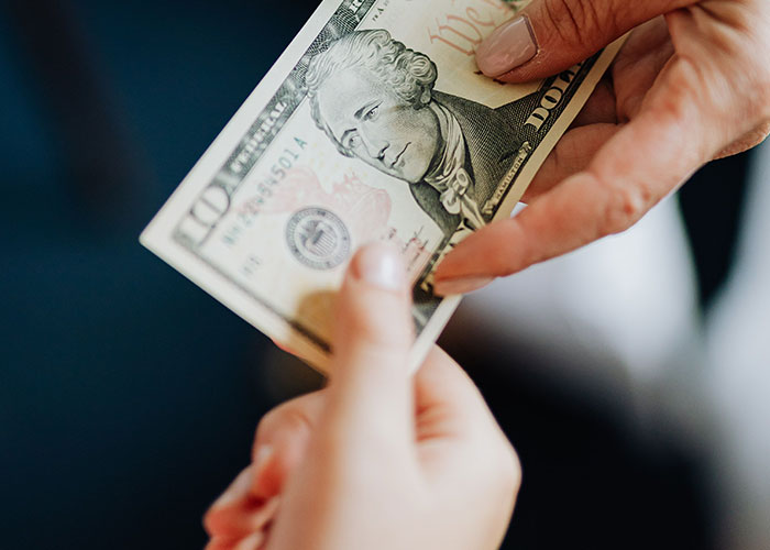 Hands exchanging money, representing payment for babysitting after an aunt invite.