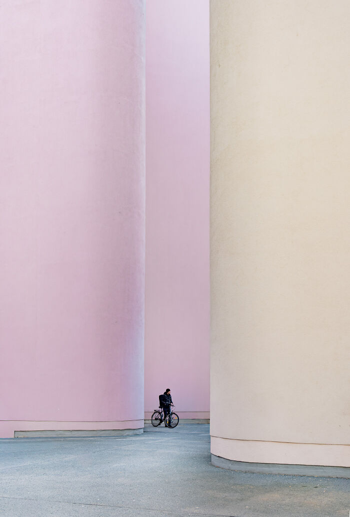 A cyclist riding between massive pink and beige curved structures, displaying the beauty of spaces