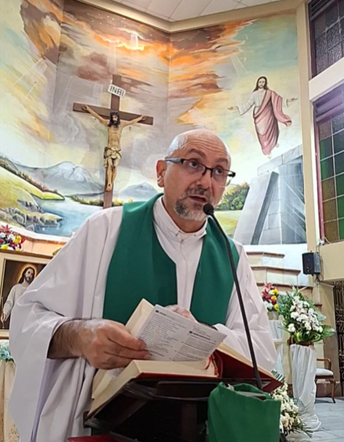 Priest reading Bible at altar with crucifix and mural behind