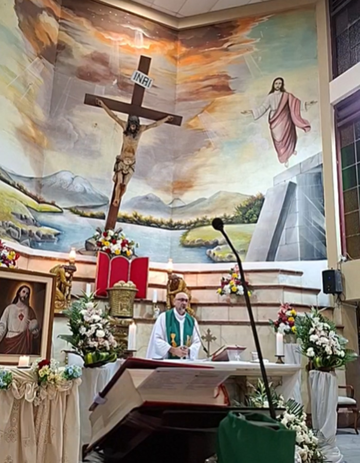 Priest conducting mass with massive crucifix and religious murals in church