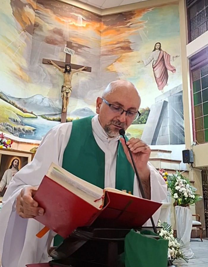 Priest reading from a book during mass with a massive crucifix on the wall behind him