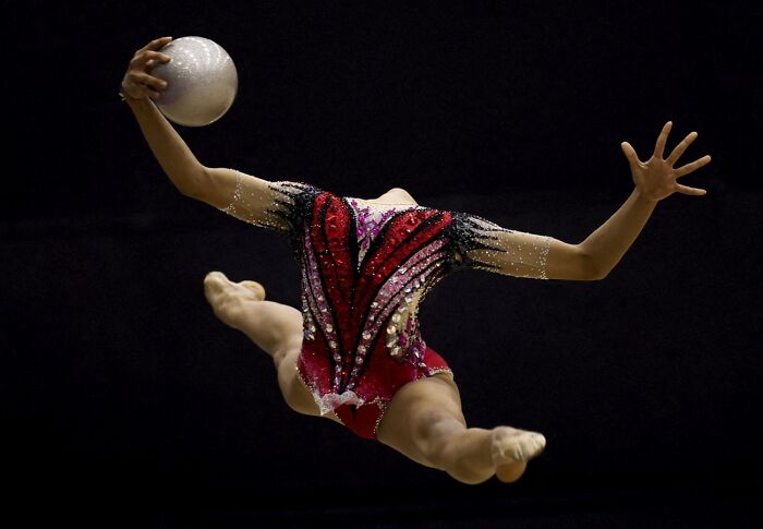 Rhythmic gymnast in mid-air performing with ball in dramatic light, best pics 2026 Siena International Photo Awards