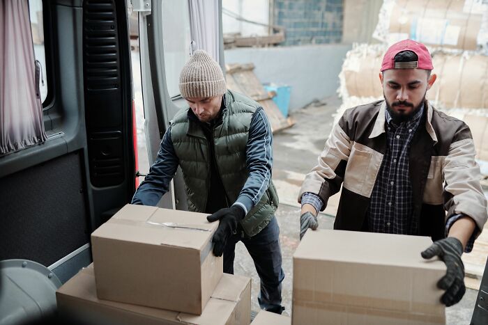 Two delivery workers loading cardboard boxes into a van, representing people who got fired early on.