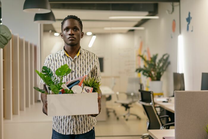 A man holding a box of personal belongings in an office after getting fired during his first week