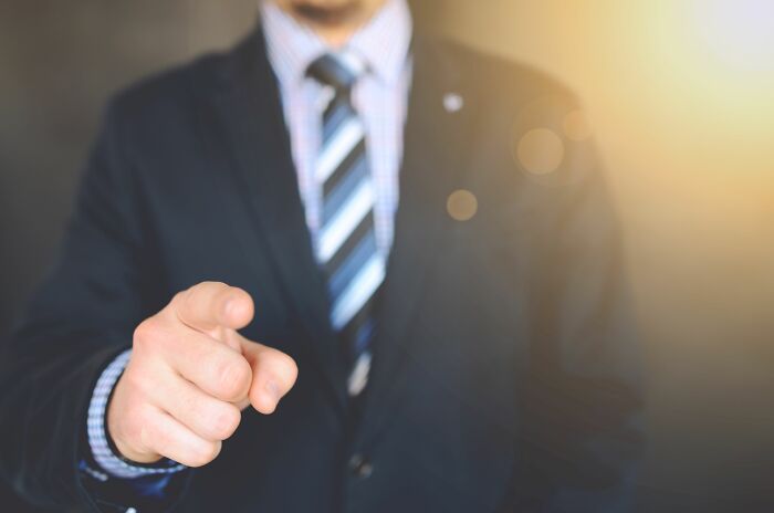 A businessman in a suit pointing directly forward, symbolizing getting fired.