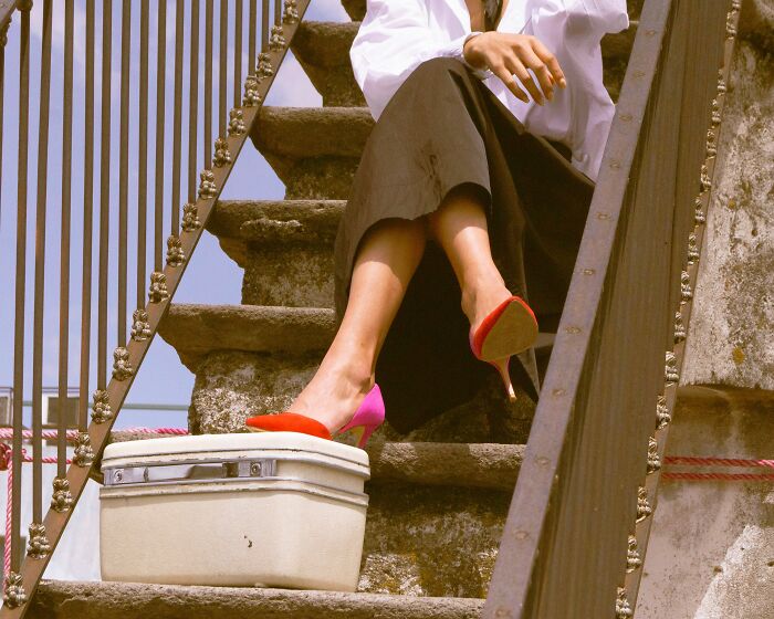 A stylish person sitting on steps with luggage, reflecting on people who got fired
