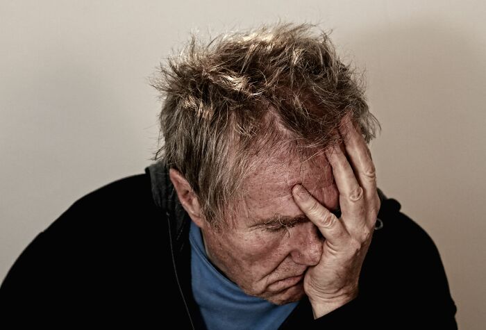 A stressed man covering his face after getting fired from his job early on