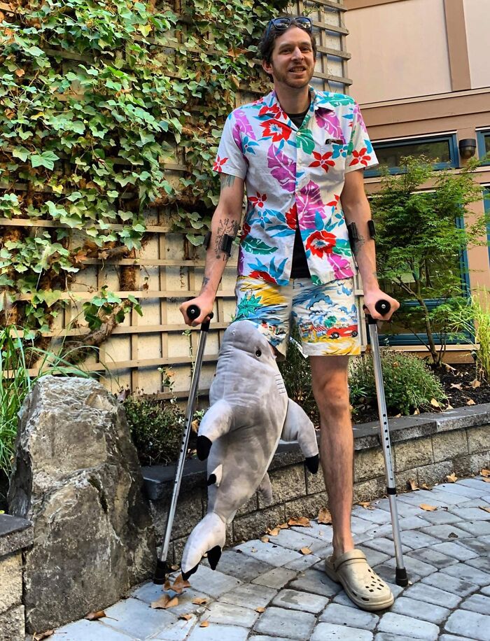 A man on crutches wearing a tropical outfit and shark accessory, representing hilarious people with disabilities.