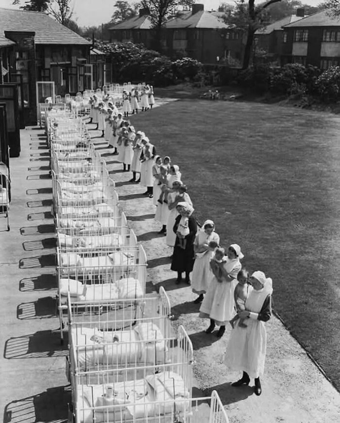 Nurses lined up with babies in cribs outside a historical orphanage
