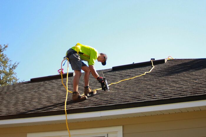 A roofing professional working on a house roof, illustrating physical work done for clients