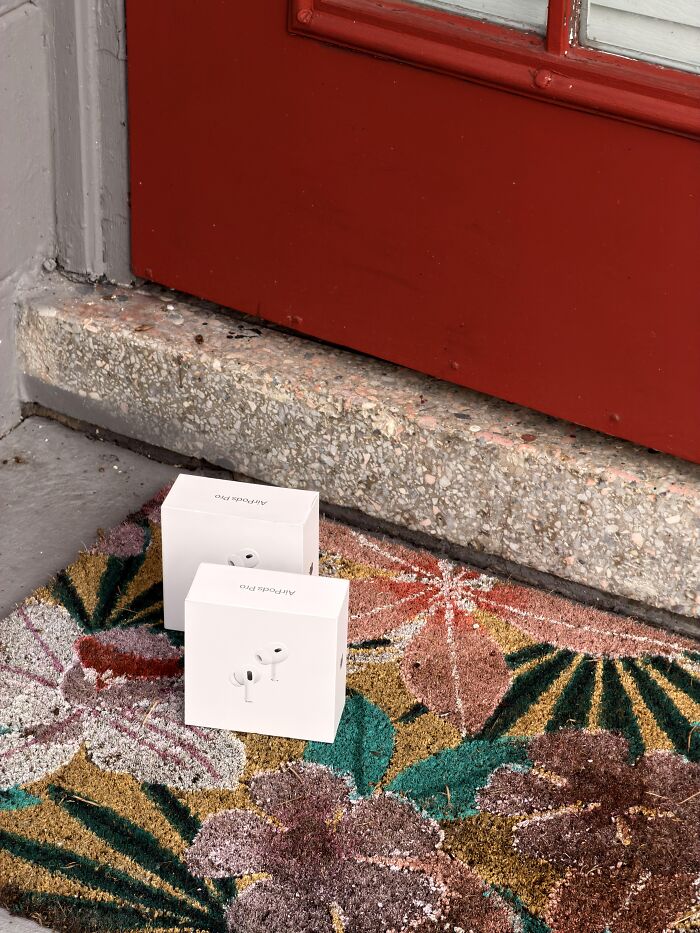 Two small package boxes sitting on a colorful doormat outside a red door.