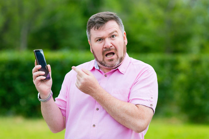 An angry man pointing at his smartphone screen, illustrating someone upset about a video recording at a state fair. An angry man pointing at his smartphone screen, illustrating someone upset about a video recording at a state fair.