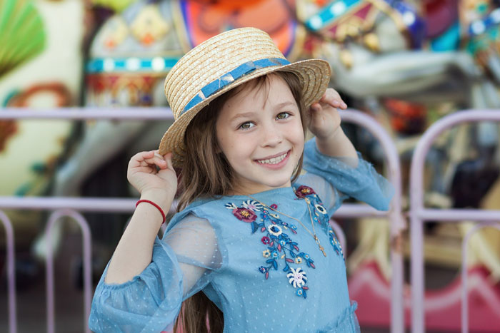 A smiling little girl in a straw hat posing near a carousel at a state fair. A smiling little girl in a straw hat posing near a carousel at a state fair.