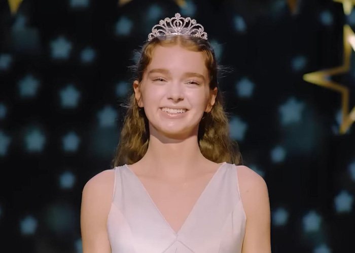 Hollywood rising star smiles while wearing a glittering tiara in Stephen King remake scene.